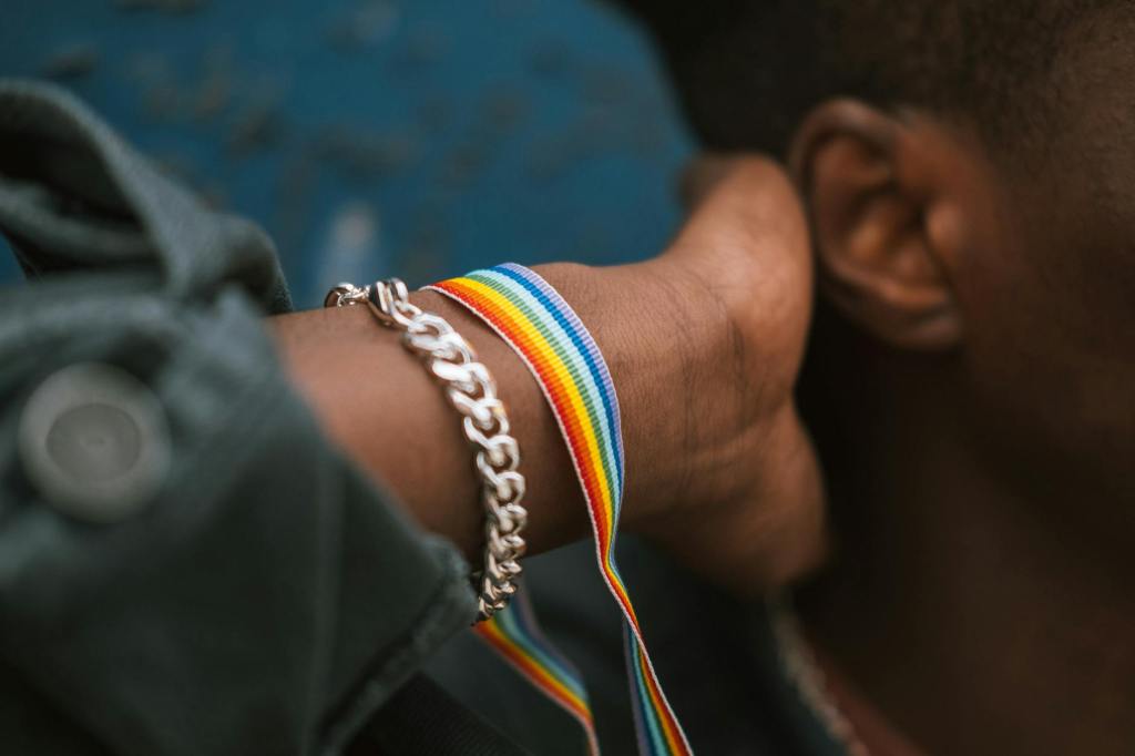 person wearing pride bracelet and touching neck